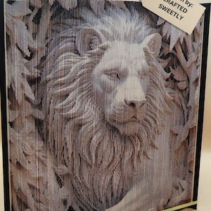 May include: A book sculpture featuring a lion's head carved from the pages. The artwork is in shades of brown and beige, with the text "Pattern by: CRAFTED SWEETLY" on a tag. The edges of the book are black with a gold trim.