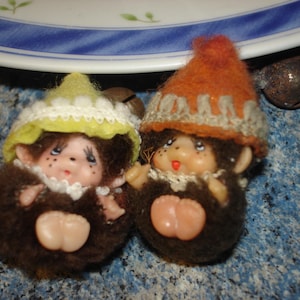 May include: Two plush monkey toys wearing hats. One monkey is wearing a yellow and white hat with a white trim. The other monkey is wearing an orange and white hat with a white trim.