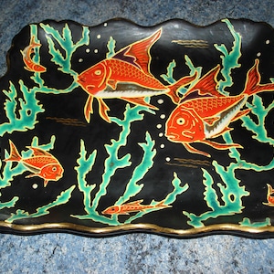 Könnte beinhalten: Eine schwarze Keramik-Schale mit goldfarbenem Rand zeigt ein Design aus orangefarbenen und roten Fischen, die zwischen grünem Seegras schwimmen. Die Schale ist mit weißen Punkten und goldenen Akzenten verziert.
