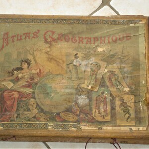 May include: A vintage wooden box with a faded, colourful illustration on the lid. The illustration depicts a woman holding a book, a globe, and various other figures. The text "ATLAS GEOGRAPHIQUE" is printed in red letters on the top of the box.