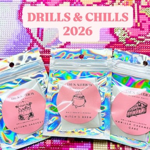 Könnte beinhalten: Drei holografische Beutel mit Duftknete, jeweils mit einem runden rosa Etikett. Die Etiketten zeigen schwarze Strichzeichnungen eines Kürbiswagens, eines Kessels und eines Kuchenstücks sowie den Text "THES STUDIOS" und "DRILLS & CHILLS 2026".