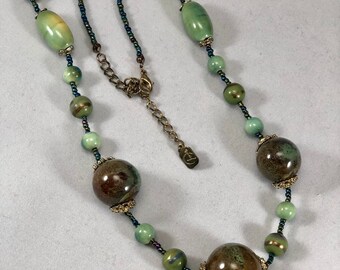 May include: A green and brown beaded necklace with a gold clasp. The necklace features large, round beads with a mottled green and brown glaze.