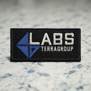 Op de afbeelding: Een witte keramische mok met een zwarte handgreep en de tekst "But First, Coffee" in een vetgedrukte, zwarte letter. De mok staat tegen een vage achtergrond, wat een gezellige omgeving suggereert.