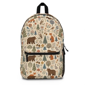 May include: A beige backpack featuring a repeating pattern of brown bears, orange foxes, grey rabbits, owls, and various birds. The design includes green pine trees, colorful flowers, mushrooms, and acorns scattered across the entire surface.