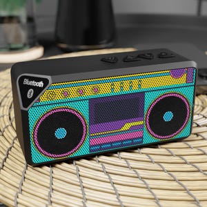 Pode incluir: Uma coluna Bluetooth retangular preta com um gráfico pop-art vibrante de um boombox no painel frontal. O design inclui cores brilhantes ciano, amarelo e magenta com um padrão de pontos, dois altifalantes circulares e um leitor de cassetes.