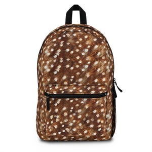 Pode incluir: Uma mochila com um padrão de pelo castanho com manchas brancas que lembra a pelagem de um cervo. A bolsa inclui um compartimento principal, um bolso frontal com fecho de correr preto, uma alça superior preta e um bolso lateral de rede preta.