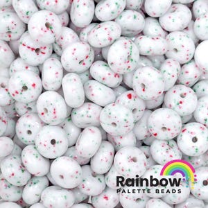 May include: A close-up of a pile of white donut-shaped beads with red and green speckles. The beads are perfect for crafting and jewelry making.