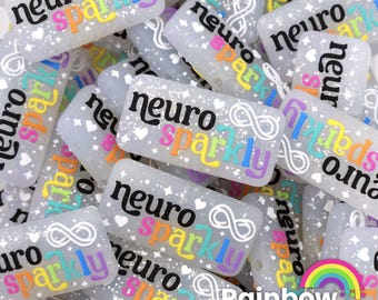 May include: A close-up of a variety of white rectangular beads with the text "neuro sparkly" in rainbow colors. The beads are scattered on a white surface.