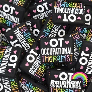 May include: A close-up of several black square-shaped buttons with the text "OT Occupational Therapist" in white and rainbow colors. Some buttons have hearts and a rainbow.