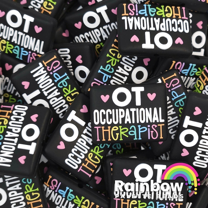May include: A close-up of several black square-shaped buttons with the text "OT Occupational Therapist" in white and rainbow colors. Some buttons have hearts and a rainbow.