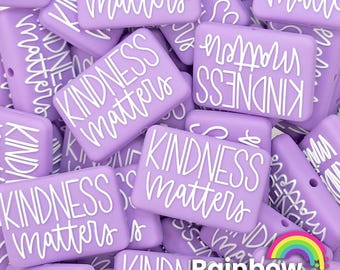 Könnte beinhalten: Nahaufnahme eines Stapels von lavendelfarbenen Silikonperlen mit dem Text "Kindness Matters" in Weiß auf jeder Perle. Die Perlen sind in einem zufälligen Muster angeordnet und alle gleich groß und geformt.