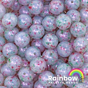 May include: Close-up of a pile of iridescent beads. The beads are round, with a light blue base color and speckled with red, green, and purple glitter. The text "Rainbow Palette Beads" is visible in the bottom right corner.