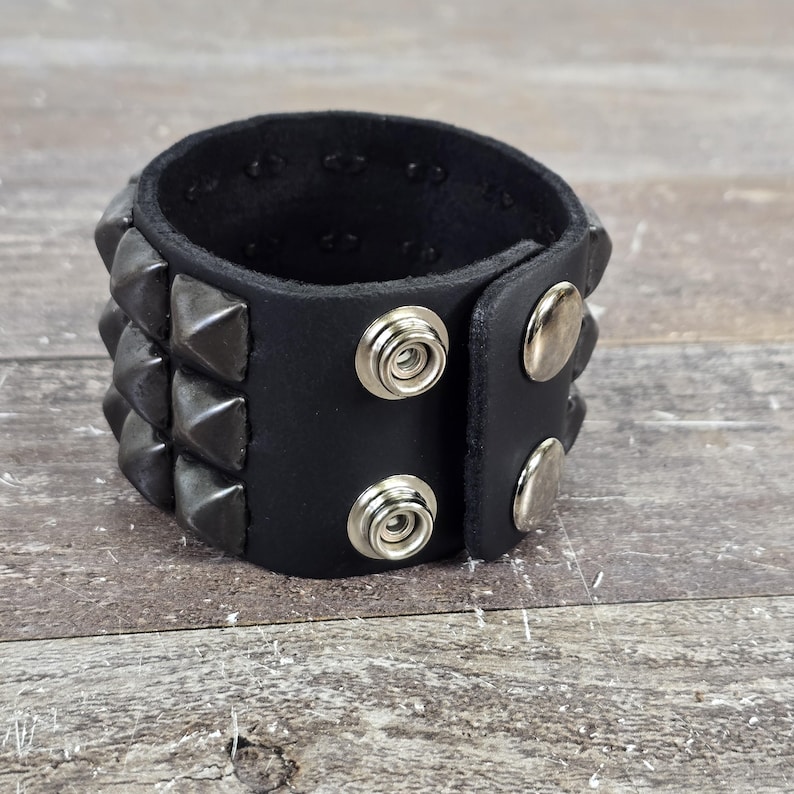 May include: A black leather bracelet with silver pyramid studs and snap closures.