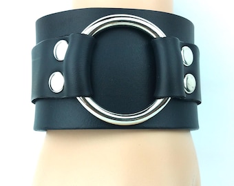 May include: Black leather bracelet with a large silver ring and silver studs.