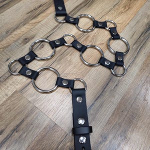 Könnte beinhalten: Schwarzer Ledergürtel mit silbernen Metallringen. Der Gürtel hat mehrere Ringe, die daran befestigt sind und ein einzigartiges und stilvolles Design schaffen.