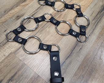 May include: Black leather belt with silver metal rings. The belt has multiple rings attached to it, creating a unique and stylish design.