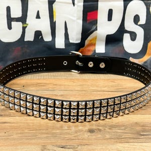 May include: A black leather belt with three rows of silver pyramid-shaped studs.