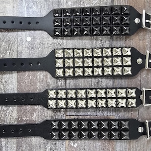 May include: Four black leather bracelets with silver and black pyramid-shaped studs. Each bracelet has a silver buckle.