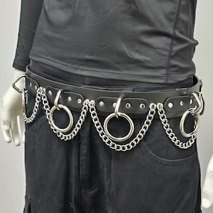 May include: Black leather belt with silver chain and ring details. The belt has multiple large metal rings and a chain design, creating a bold, edgy aesthetic. The belt is secured with a metal buckle.