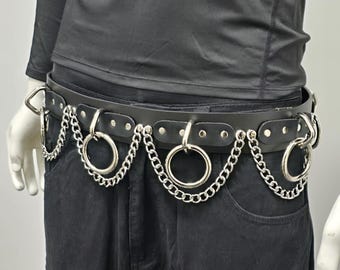 May include: Black leather belt with silver-colored chain and ring accents. The belt features multiple large metal rings and a chain design, creating a bold, edgy aesthetic. The belt is secured with a metal buckle.