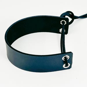 May include: A black leather headband with two silver metal eyelets and a black elastic strap.
