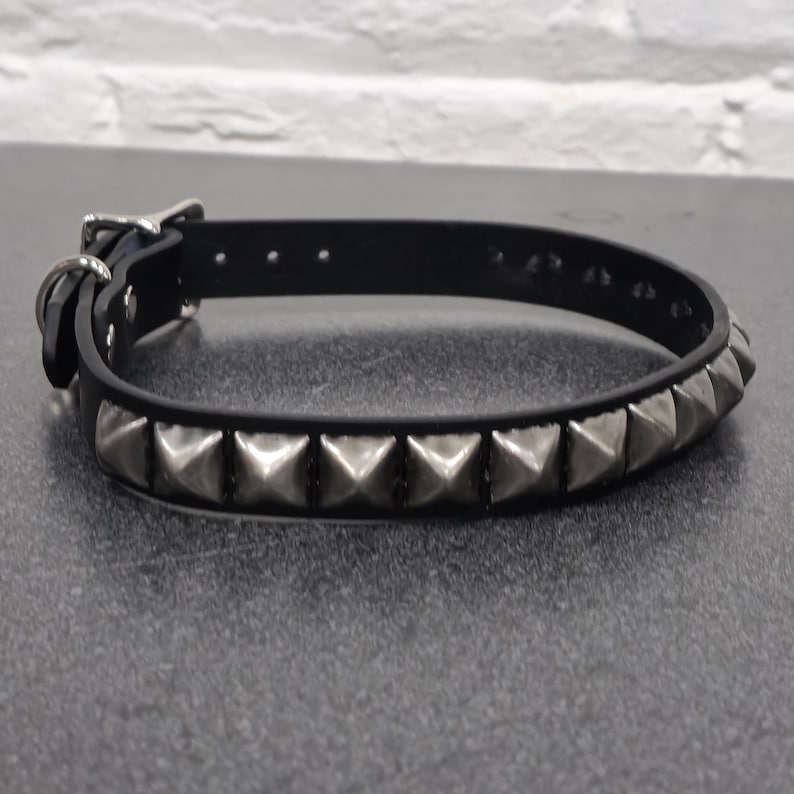 May include: Black leather collar with silver pyramid studs. The collar has a buckle closure and a metal loop. The studs are evenly spaced along the collar's length, creating a bold, edgy look. The collar is designed for pets.