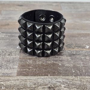 May include: A black leather bracelet with three rows of pyramid-shaped studs.