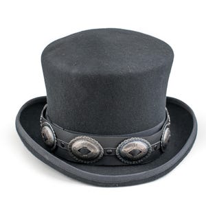May include: A black top hat with a wide brim. The hat features a black leather band adorned with silver-colored oval embellishments. The hat is made of a felt-like material and is set against a white background.