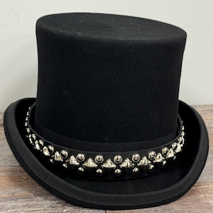 Puede incluir: Un sombrero de copa negro con una banda de tachuelas plateadas alrededor del borde.