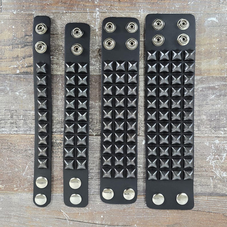 May include: Four black leather bracelets with silver pyramid studs. The bracelets are different lengths and have silver snap closures.