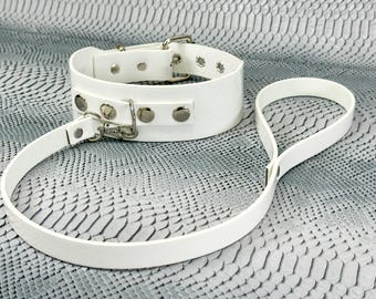 May include: White leather collar and leash set with silver hardware. The collar is wide and has multiple rows of silver studs. The leash is thin and has a simple design.