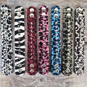 May include: Seven faux fur bracelets with silver studs and a leopard print design. The bracelets are in black and white, red, pink, blue, green, and white.