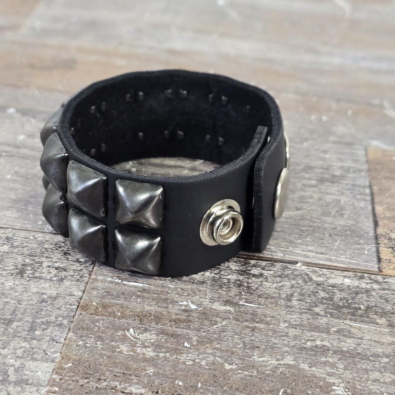 May include: A black leather bracelet with silver pyramid-shaped studs. The bracelet has a snap closure.