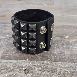 May include: Black leather cuff bracelet with silver pyramid studs and two silver snap closures.