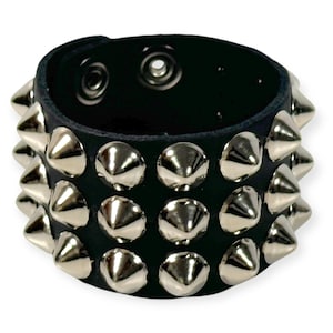 Puede incluir: Pulsera de cuero negro con tres filas de tachuelas piramidales plateadas.