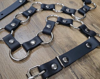 May include: A black leather belt with silver metal rings and studs. The belt has a buckle closure.