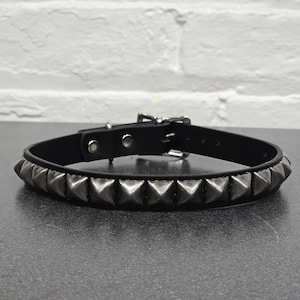 May include: A black leather collar with silver pyramid studs. The collar has a buckle closure.