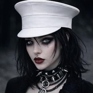 May include: A crisp white military-style cap with a structured brim and flat top. The accessory features a smooth finish and a clean, minimalist design, providing a stark contrast to the dark aesthetic of the wearer's black spiked choker and chains.