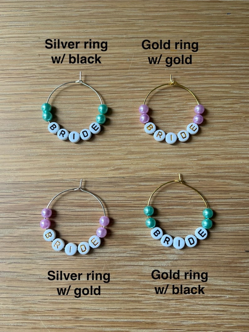 May include: Four circular hoop rings featuring white letter beads spelling BRIDE. The top left is a silver ring with teal beads, top right is a gold ring with pink beads, bottom left is a silver ring with pink beads, and bottom right is a gold ring with teal beads.