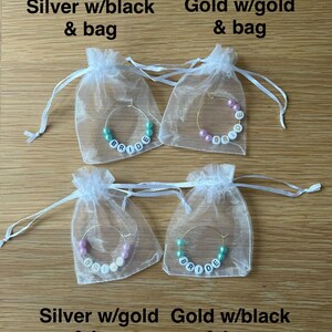 May include: Four hoop earrings with white letter beads spelling BRIDE, each inside a sheer white drawstring bag. The top left is silver with teal beads, top right is gold with pink beads, bottom left is silver with pink beads, bottom right is gold with teal beads.