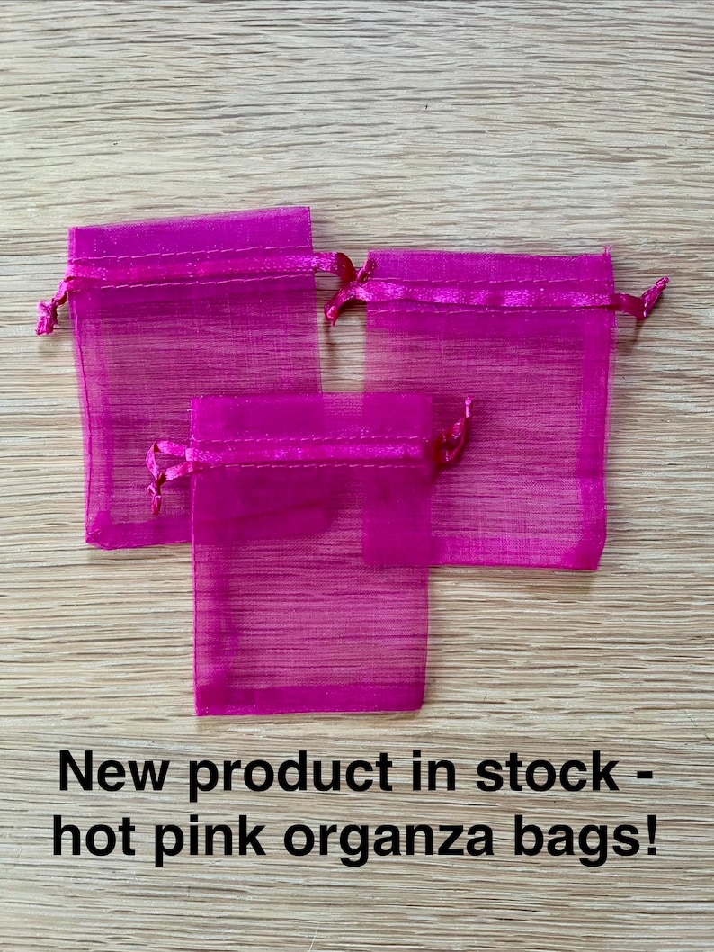 May include: Three hot pink organza drawstring bags with a sheer, semi-transparent fabric texture. The bags feature a matching ribbon closure at the top. The text "New product in stock - hot pink organza bags!" is printed in black at the bottom.