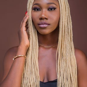 May include: A woman with long, blonde braids wearing a black top. She is looking at the camera with a serious expression. Her nails are painted red.