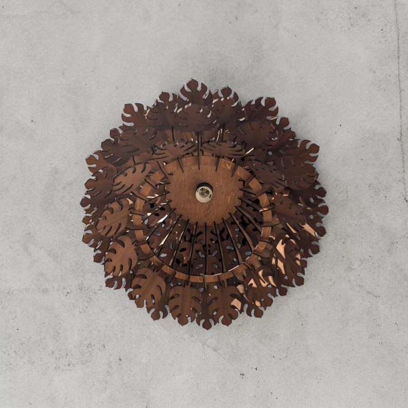 May include: A brown, circular ceiling light fixture with a leaf-like design. The light fixture is made of layered, laser-cut wood and features a central light bulb. The fixture is mounted on a gray ceiling.