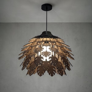 May include: A pendant light fixture with a black ceiling mount and cord. The lampshade is made of layered, laser-cut wooden leaves in a natural wood tone. The light is on, illuminating the leaf pattern.
