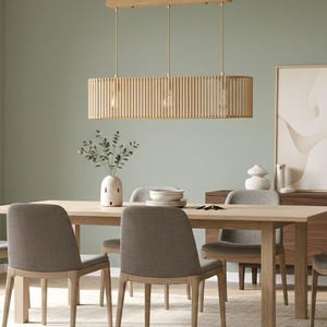 Può includere: Una sala da pranzo con un tavolo in legno chiaro e sedie imbottite grigie. Una lampada a sospensione rettangolare in legno è appesa sopra il tavolo. Un vaso con vegetazione e un'opera d'arte incorniciata completano la scena.