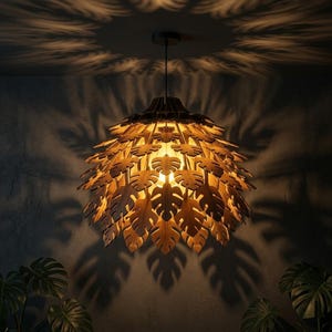 May include: A wooden pendant light fixture with a leaf design. The light is suspended from the ceiling and casts leaf-shaped shadows on the wall. The fixture has a warm, inviting glow, and the leaves are intricately cut.