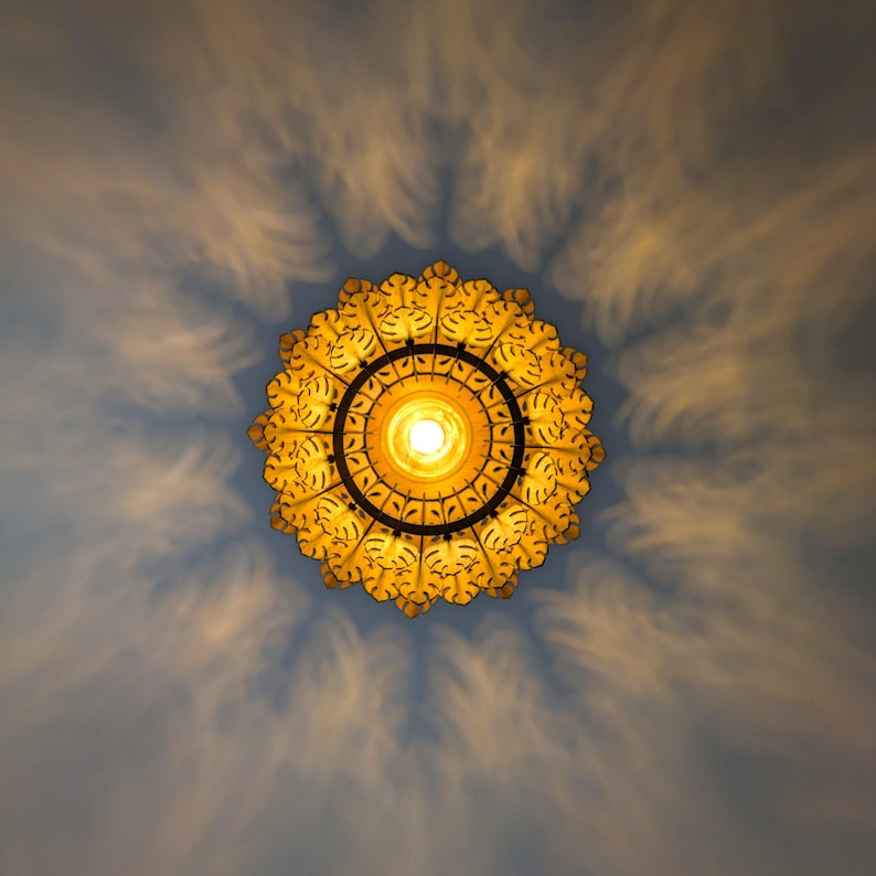 May include: A decorative, ornate ceiling light fixture with a circular design. The light is yellow and casts a pattern of shadows on the blue ceiling. The fixture has a detailed, floral-like pattern around the central light source.