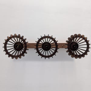 May include: A wooden wall-mounted light fixture featuring three circular, dark brown, spoked shades. The shades are attached to a horizontal wooden beam. The fixture is designed to be mounted on a wall.