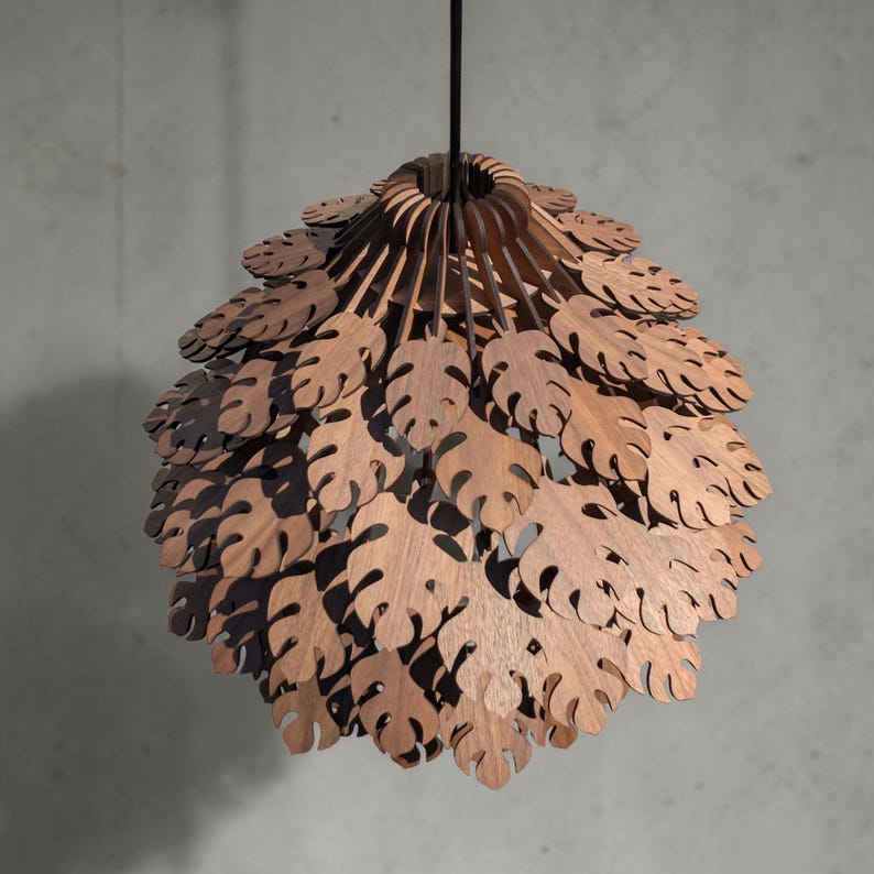 May include: A wooden pendant light fixture with a layered design. The light features a series of leaf-shaped cutouts, creating a natural, organic aesthetic. The fixture is suspended from a black cord, offering a warm, inviting glow.