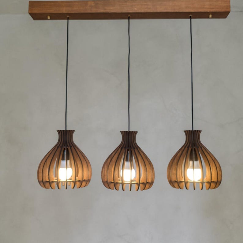 May include: Three pendant lights with wooden shades. Each shade has a teardrop shape with vertical wooden slats. The lights hang from a rectangular wooden beam. The bulbs are visible inside the shades, emitting a warm glow.